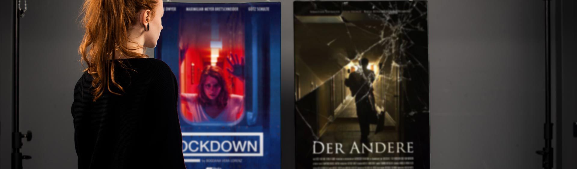 Photography of Nina Lesznik standing in front of hanging posters showing her Production Design Projects "Lockdown" and "Der Andere"