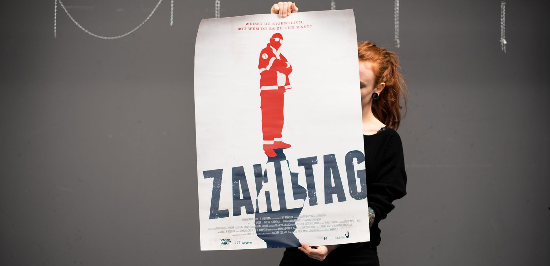 Photography of Nina Lesznik holding a lange film poster of her production design project "Zahltag"