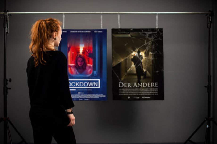 Photography of Nina Lesznik standing in front of hanging posters showing film posters of "Lockdown" and "Der Andere"